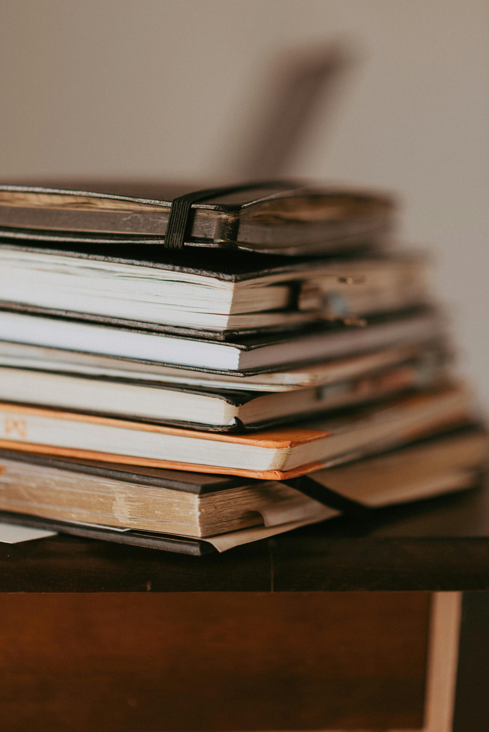 Close-up of stacked notebooks on a wooden table with warm lighting.