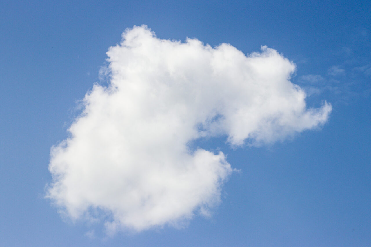 A solitary white cloud floats against a vibrant blue sky on a clear day.
