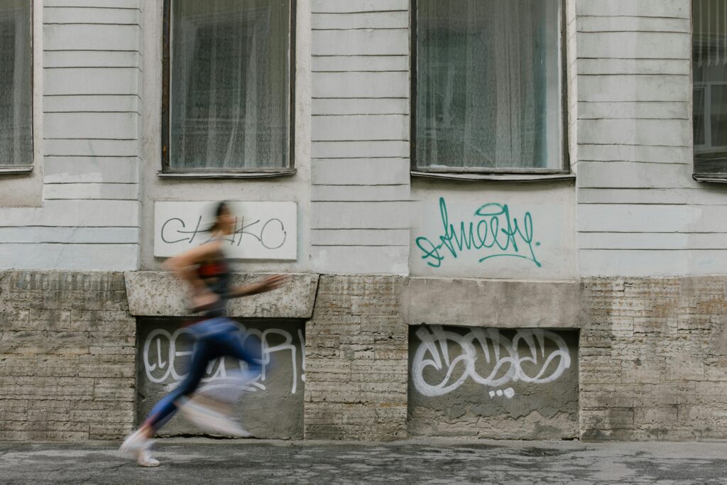 Blurred motion of a woman running past a graffiti-covered urban wall. Captures dynamic energy.