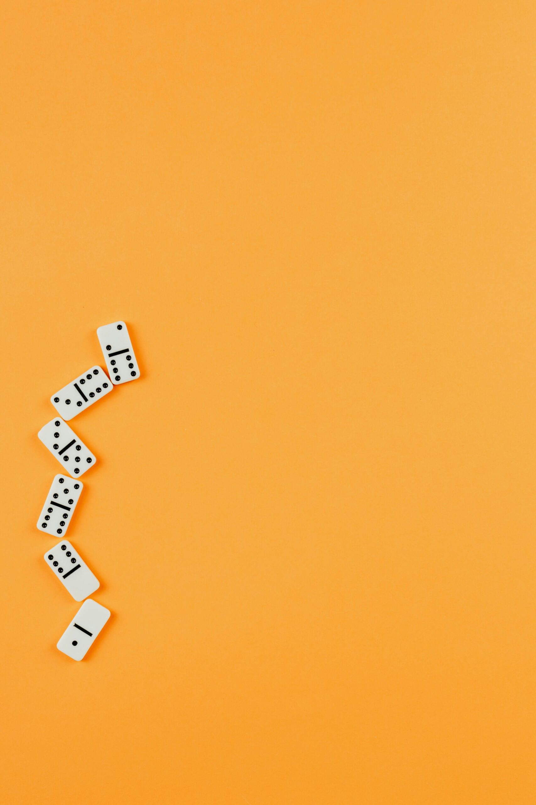A flat lay of domino pieces arranged artistically on a bright orange backdrop, showcasing clean and simple design.