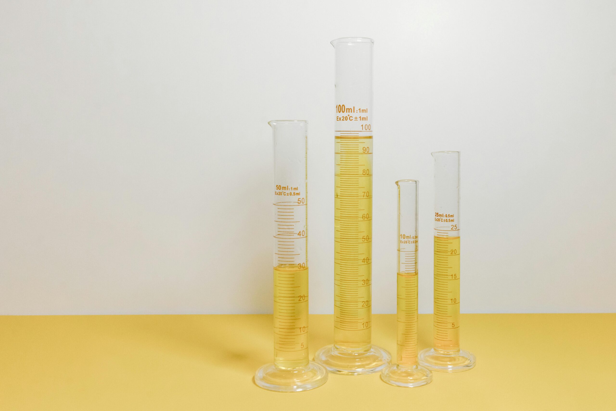 Four graduated cylinders filled with yellow liquid on a yellow background, showcasing laboratory equipment.